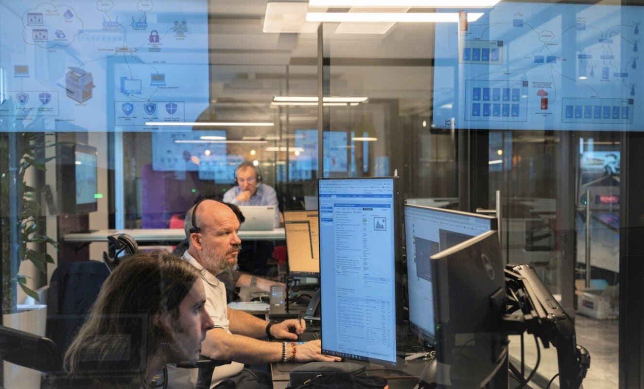des salariés devant leurs ordinateurs en train de travailler, réflexion des écrans sur la vitre au premier plan de l'image